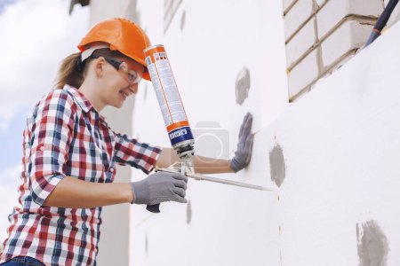 Photo for Insulation of the house with polyfoam. The woman worker foaming joints of polystyrene board on the facade. - Royalty Free Image