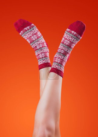 Photo for Female legs in christmas socks on orange background - Royalty Free Image
