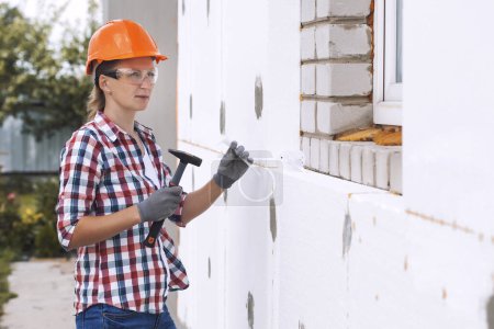Photo for Insulation of the house with polyfoam. The woman worker is checking with the construction level the accuracy of the installation of polystyrene board on the facade. - Royalty Free Image