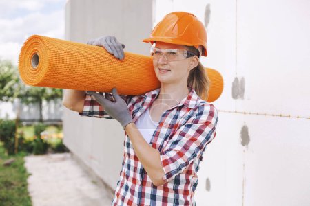 Foto de La trabajadora con rollos de fibra de vidrio reforzada. Aislamiento de la casa con tablero de poliespuma en la fachada - Imagen libre de derechos