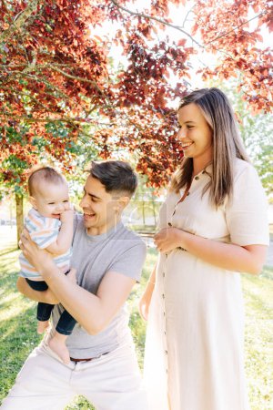 Retrato de una familia joven con su bebé de nueve meses divirtiéndose en el parque público