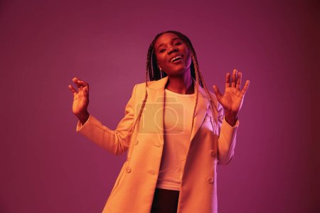 Téléchargez les photos : Femme afro-américaine entreprise sourire danse fête dans la lumière au néon, couleur rose coloré, coloration lumineuse. Photo de haute qualité - en image libre de droit
