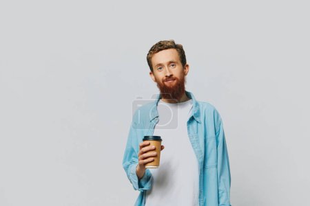 Téléchargez les photos : Homme hipster avec une tasse de café avec un sourire sur un fond gris dans une chemise bleue et t-shirt blanc. Photo de haute qualité - en image libre de droit