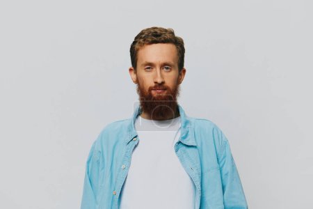 Téléchargez les photos : Homme hipster portrait sourire sur fond gris en chemise bleue et t-shirt blanc, portrait d'un homme avec une barbe. Photo de haute qualité - en image libre de droit