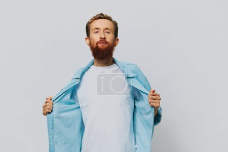 Téléchargez les photos : Homme hipster portrait sourire sur fond gris en chemise bleue et t-shirt blanc, portrait d'un homme avec une barbe. Photo de haute qualité - en image libre de droit