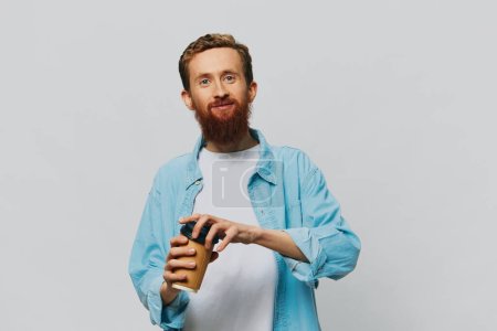 Téléchargez les photos : Homme hipster avec une tasse de café avec un sourire sur un fond gris dans une chemise bleue et t-shirt blanc. Photo de haute qualité - en image libre de droit