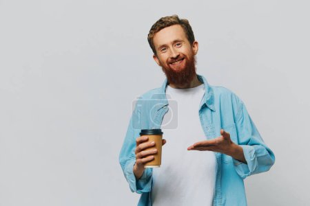 Foto de Hombre hipster con una taza de café con una sonrisa sobre un fondo gris en una camisa azul y camiseta blanca. Foto de alta calidad - Imagen libre de derechos