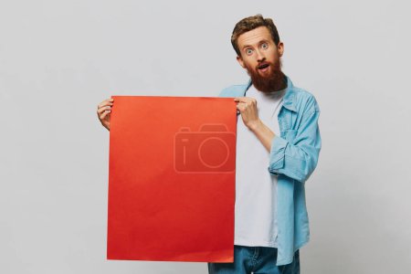 Téléchargez les photos : Portrait d'un homme adulte sur fond gris avec un morceau de papier rouge pour votre conception et texte, mise en page, espace de copie, espace pour le texte. Photo de haute qualité - en image libre de droit