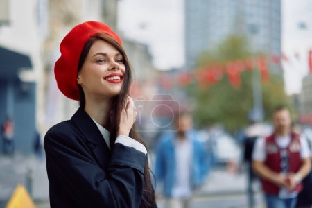 Téléchargez les photos : Une belle femme souriante avec des dents se promène dans la ville sur fond d'immeubles de bureaux, de vêtements et de maquillage vintage à la mode, de marche d'automne, de voyage. Photo de haute qualité - en image libre de droit