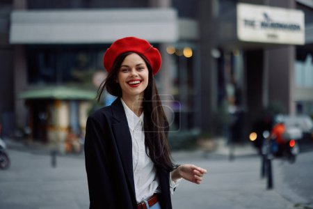 Téléchargez les photos : Femme sourire avec des dents promenades touristiques promenades dans la ville sur le fond des immeubles de bureaux, vêtements élégants à la mode et maquillage, marche de printemps, Voyage. Photo de haute qualité - en image libre de droit