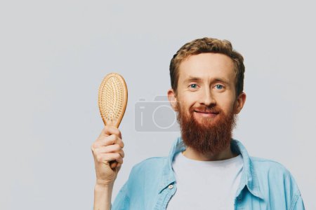 Foto de Retrato de un hombre con un peine de masaje en las manos, peinándose el pelo y la barba, problema de pérdida de cabello. Foto de alta calidad - Imagen libre de derechos
