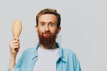 Téléchargez les photos : Portrait d'un homme avec un peigne de massage dans ses mains, peigner ses cheveux et sa barbe, problème de perte de cheveux. Photo de haute qualité - en image libre de droit