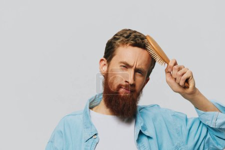 Photo for Portrait of a man with a massage comb in his hands, combing his hair and beard, hair loss problem. High quality photo - Royalty Free Image