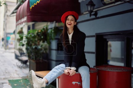 Téléchargez les photos : Femme assise devant un café et un bar dans une rue de la ville, image de mode élégante de vêtements, vacances et voyages, promenade en ville. Photo de haute qualité - en image libre de droit