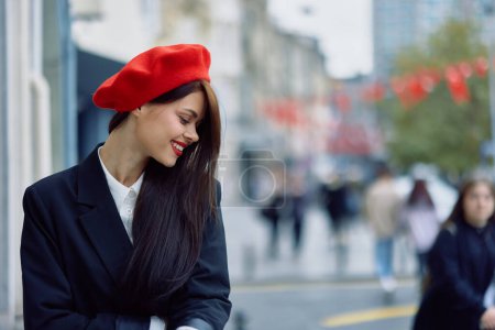 Téléchargez les photos : Une belle femme souriante avec des dents se promène dans la ville sur fond d'immeubles de bureaux, de vêtements et de maquillage vintage à la mode, de marche d'automne, de voyage. Photo de haute qualité - en image libre de droit