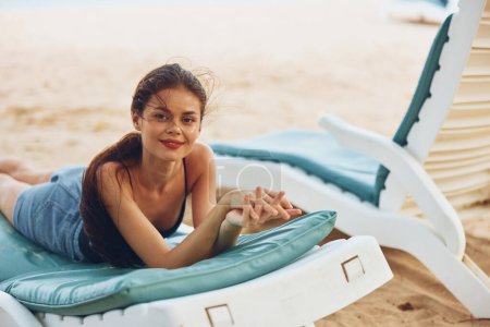 Foto de Mujer descansando sol agua arena sonriente bikini resort joven silla mar largo mujer playa pelo acostado vacaciones sunbed chica gafas de sol océano estilo de vida - Imagen libre de derechos