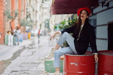 Foto de Una hermosa mujer sonriendo con los dientes se encuentra fuera de un café en una calle de la ciudad, un aspecto elegante de la moda de la ropa, vacaciones y viajes. Foto de alta calidad - Imagen libre de derechos