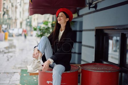 Photo for Cheerful woman smile with teeth sitting outside a cafe and bar on a city street, stylish fashion look of clothes, vacation and travel. High quality photo - Royalty Free Image