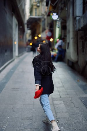 Téléchargez les photos : Femme de mode touristique en vêtements élégants dans une veste et béret rouge courant dans la rue étroite de la ville sourire et voyage de bonheur, style français, couleur cinématographique. Photo de haute qualité - en image libre de droit