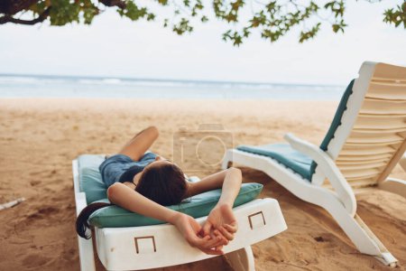 Foto de Resort mujer vacaciones mar sonriente océano arena exótica persona acostado viaje sunbed tropical sol bronceado verano relajación traje de baño azul estilo de vida playa - Imagen libre de derechos
