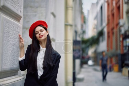 Téléchargez les photos : Femme debout près d'un mur dans la ville portant une veste élégante et béret rouge avec lèvres rouges, Voyage et loisirs, style français de robe, printemps. Photo de haute qualité - en image libre de droit