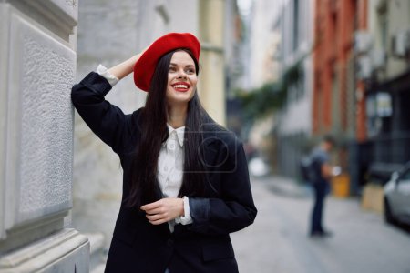 Foto de Mujer de pie cerca de una pared en la ciudad con una chaqueta elegante y boina roja con labios rojos, viajes y ocio, estilo francés de vestido. Foto de alta calidad - Imagen libre de derechos