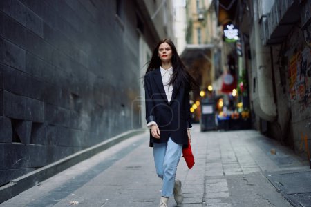 Photo for Fashion woman tourist in stylish clothes in a jacket and red beret walking down a narrow city street flying hair and happy travel, French style, cinematic color, retro style. High quality photo - Royalty Free Image