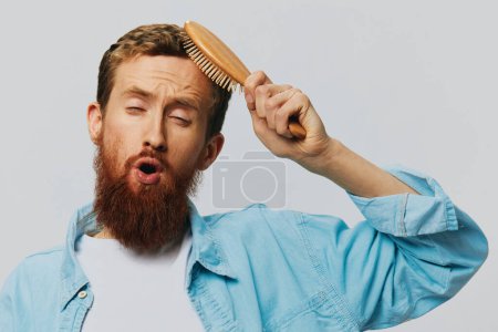 Téléchargez les photos : Portrait d'un homme avec un peigne de massage dans ses mains, peigner ses cheveux et sa barbe, problème de perte de cheveux. Photo de haute qualité - en image libre de droit
