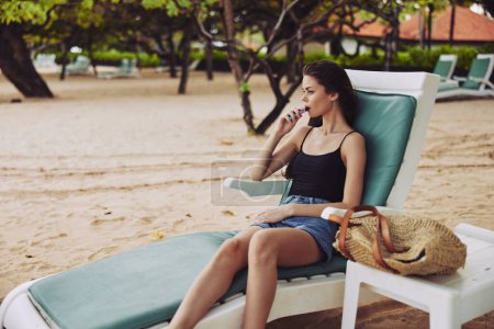 Téléchargez les photos : Femme exotique couché plage de sable d'été profiter de la mer loisirs océan jeune souriant repos chapeau sunbed style de vie vacances attrayant station soleil bikini - en image libre de droit