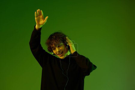 Photo for Man party with headphones listening to music, dancing and singing, DJ teenager happiness and smile, hipster lifestyle, portrait green background mixed neon light, copy space. High quality photo - Royalty Free Image