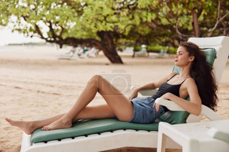 Téléchargez les photos : Femme jeune mer détente assis sourire vacances sable transat bronzage exotique loisirs resort chaise personne attrayant allongé cheveux longs plage style de vie océan - en image libre de droit