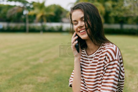 Téléchargez les photos : Femme souriante parc naturel téléphone blogueur palmier herbe en utilisant l'arbre assis appel extérieur mobile sain jeune marche application réseau mode de vie heureux adulte - en image libre de droit