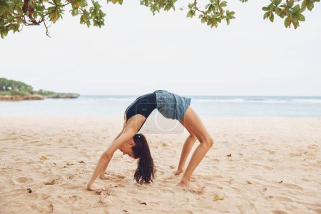 Téléchargez les photos : Femme bikini pose exercice pont gymnastique mode de vie actif yoga étirement jeune beauté été entraînement corps calme femelle sport méditation sain plage - en image libre de droit