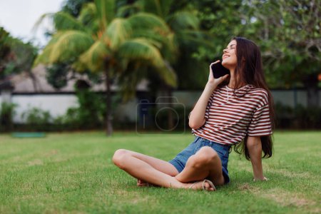 Photo for Woman blogger smart summer park seasonal grass nature tree phone cell lifestyle happy spring smiling caucasian call palm cellphone bag application girl - Royalty Free Image