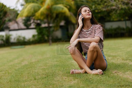 Photo for Woman cell network phone young browsing seasonal happy working grass lifestyle palm smiling adult smile t-shirt blogger tree striped park nature cellphone - Royalty Free Image
