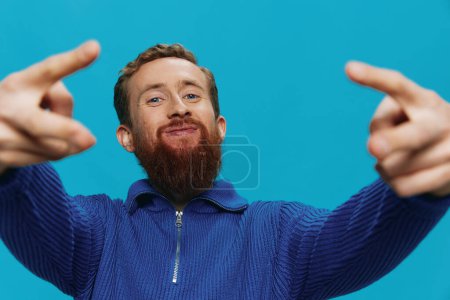 Foto de Retrato de un hombre con una sonrisa de suéter y felicidad, signos de mano y símbolos, sobre un fondo azul. Estilo de vida positivo, lugar de copia. Foto de alta calidad - Imagen libre de derechos