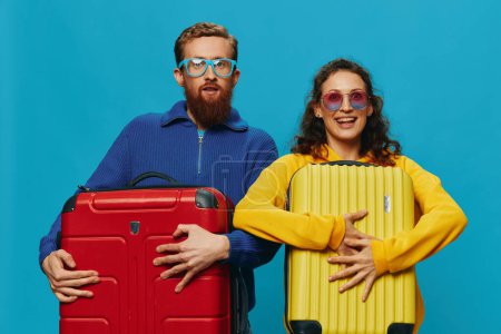 Foto de Mujer y hombre sonríen maletas en la mano con amarillo y rojo maleta sonrisa diversión, sobre fondo azul, embalaje para un viaje, viaje de vacaciones familiares. Foto de alta calidad - Imagen libre de derechos