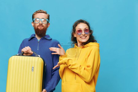 Téléchargez les photos : Femme et homme sourient assis sur une valise avec un sourire jaune, sur fond bleu, emballage pour le voyage, voyage de vacances en famille. Photo de haute qualité - en image libre de droit