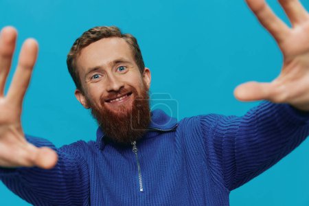 Téléchargez les photos : Portrait d'un homme en pull sourire et bonheur, signes et symboles de la main, sur fond bleu. Style de vie positif, endroit de copie. Photo de haute qualité - en image libre de droit