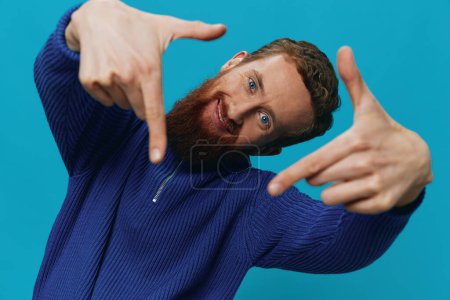 Foto de Retrato de un hombre con una sonrisa de suéter y felicidad, signos de mano y símbolos, sobre un fondo azul. Estilo de vida positivo, lugar de copia. Foto de alta calidad - Imagen libre de derechos