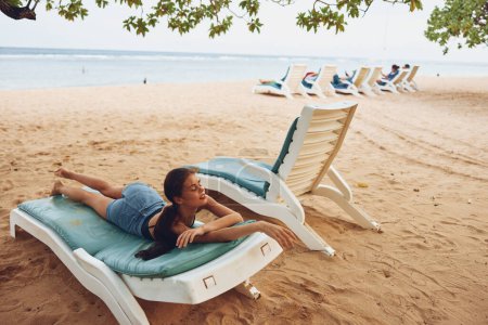Téléchargez les photos : Femme relax chaise transat plage bikini vacances assis bronzage caucasien couché sourire mer océan repos eau sable repos jeune lifestyle resort - en image libre de droit