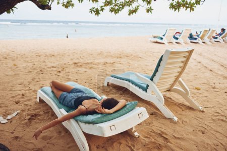 Foto de Mujer tumbona playa tumbada agua playa sonriente sol exótico traje de baño persona silla gafas de sol mar arena disfrutar de vacaciones de descanso hermoso resort océano estilo de vida - Imagen libre de derechos