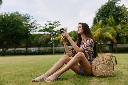 Photo for Woman lifestyle tree network beautiful park blogger smartphone grass happy healthy caucasian human nature phone palm smiling striped talk outdoor young seasonal - Royalty Free Image
