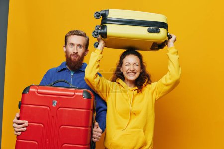 Photo for Woman and man smiling, suitcases in hand with yellow and red suitcase smiling merrily and crooked, yellow background, going on a trip, family vacation trip, newlyweds. High quality photo - Royalty Free Image
