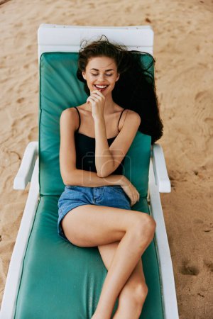 Foto de Descansando mujer playa sentado mar bronceado sombrero persona bikini acostado vacaciones resort sunbed exótico sol océano morena sonriente estilo de vida vacaciones arena - Imagen libre de derechos