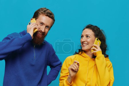 Téléchargez les photos : Femme et homme couple joyeux avec des téléphones dans leurs mains sourire tordu joyeux, sur fond bleu. Le concept de vraies relations familiales, parler au téléphone, travailler en ligne. Photo de haute qualité - en image libre de droit