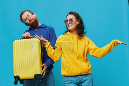 Foto de Mujer y hombre sonríen sentados en la maleta con una sonrisa amarilla en la maleta, sobre un fondo azul, empacando para el viaje, viaje de vacaciones en familia. Foto de alta calidad - Imagen libre de derechos