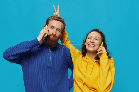 Foto de Mujer y hombre alegre pareja con teléfonos en sus manos sonrisa torcida alegre, sobre fondo azul. El concepto de relaciones familiares reales, hablar por teléfono, trabajar en línea. Foto de alta calidad - Imagen libre de derechos