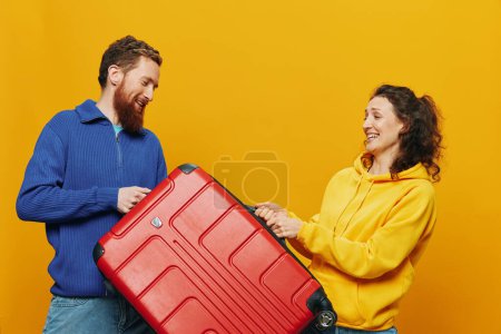 Téléchargez les photos : Femme et homme souriant, valises à la main avec valise jaune et rouge souriant joyeusement et tordu, fond jaune, aller en voyage, voyage de vacances en famille, jeunes mariés. Photo de haute qualité - en image libre de droit