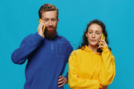 Foto de Mujer y hombre alegre pareja con teléfonos en sus manos sonrisa torcida alegre, sobre fondo azul. El concepto de relaciones familiares reales, hablar por teléfono, trabajar en línea. Foto de alta calidad - Imagen libre de derechos